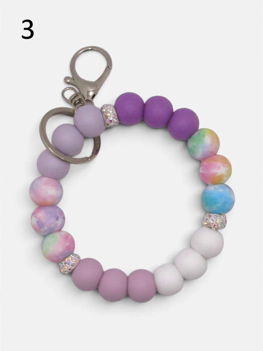 Flutterby Creations beadable wristlet featuring purple, white, and pastel tie-dye silicone beads with crystal accents.