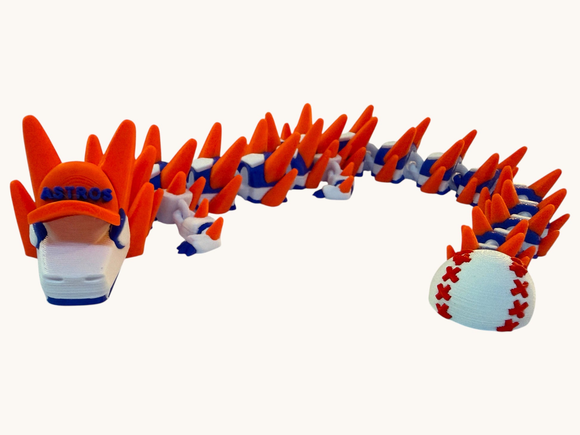 Flutterby Creations 3D printed dragon toy in orange, blue, and white, wearing an Astros baseball cap and with a baseball-tipped tail.