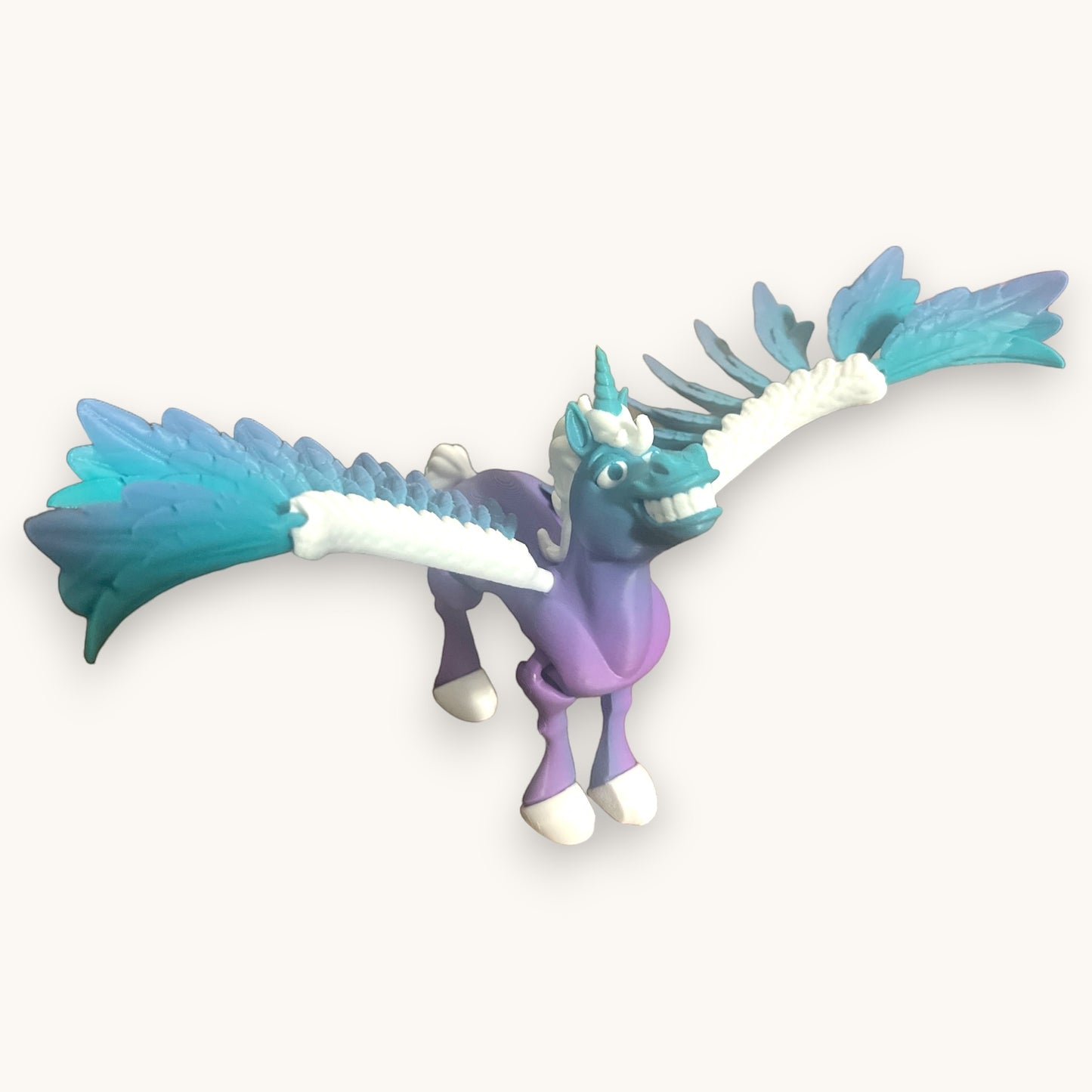 Flutterby Creations Flexicorn 3D printed toy unicorn with purple body, blue wings, and a toothy grin.