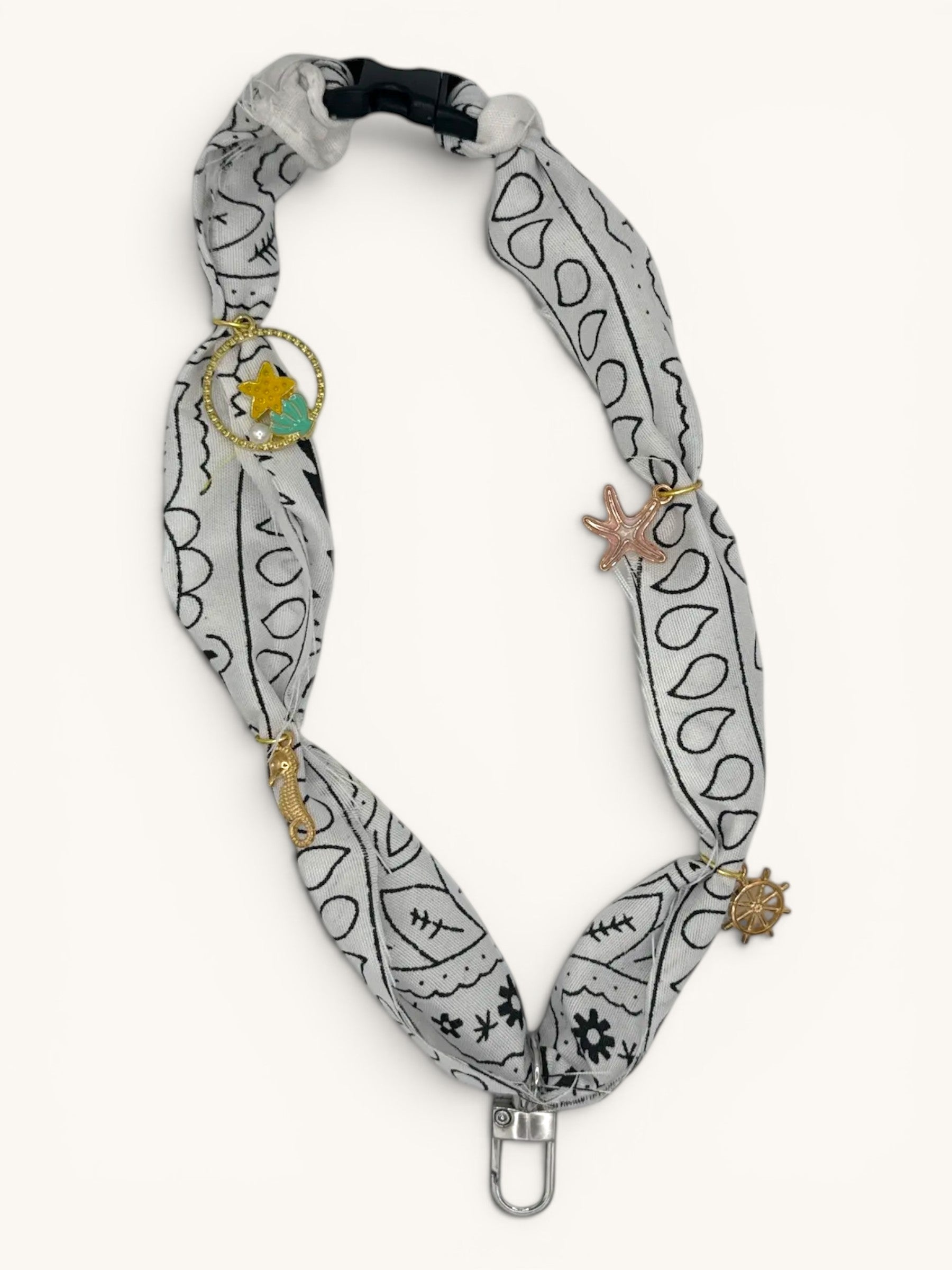 Flutterby Creations Freshie Hanger with a grey bandana print fabric, gold charms of a seahorse, starfish, ship wheel, and a star with teal accent.