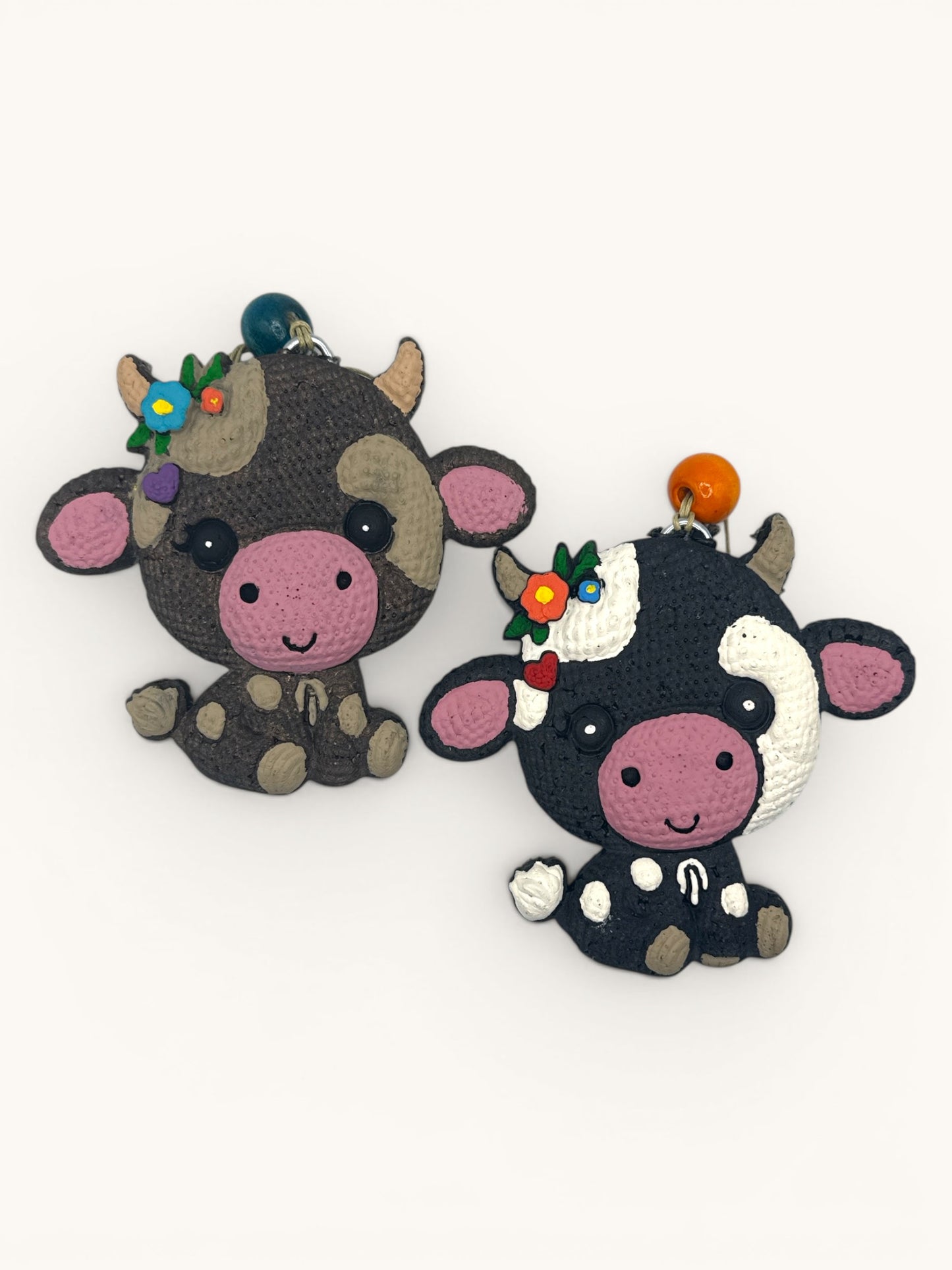 Flutterby Creations knitted cow freshies, one brown and grey, one black and white, with floral accents and beaded hangers.