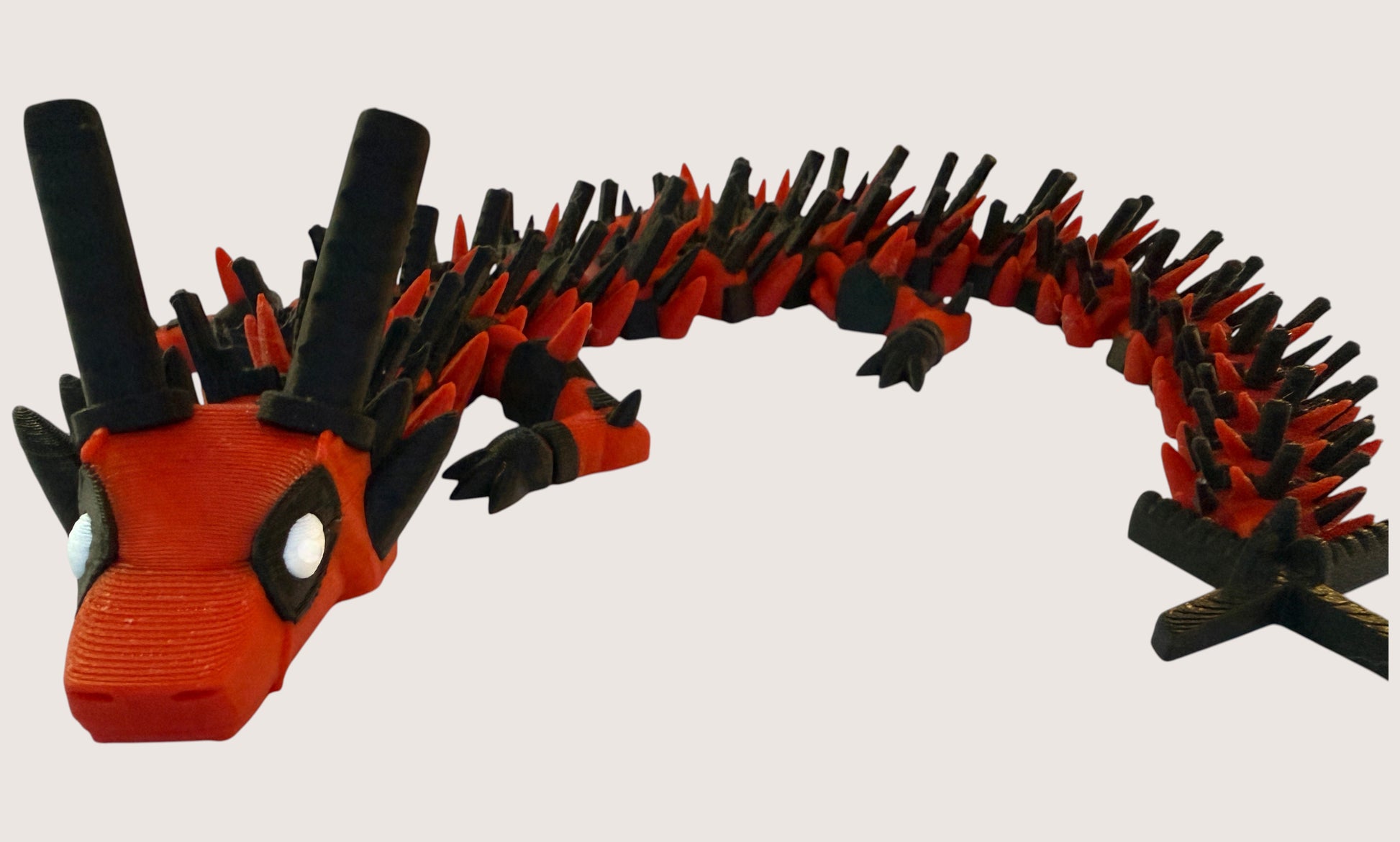 Flutterby Creations red and black 3D printed flexible dragon toy with white eyes and black horns.