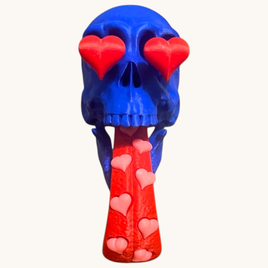 Flutterby Creations blue 3D printed skull with red heart eyes and a red tongue adorned with pink hearts. Can be used as a pen holder.