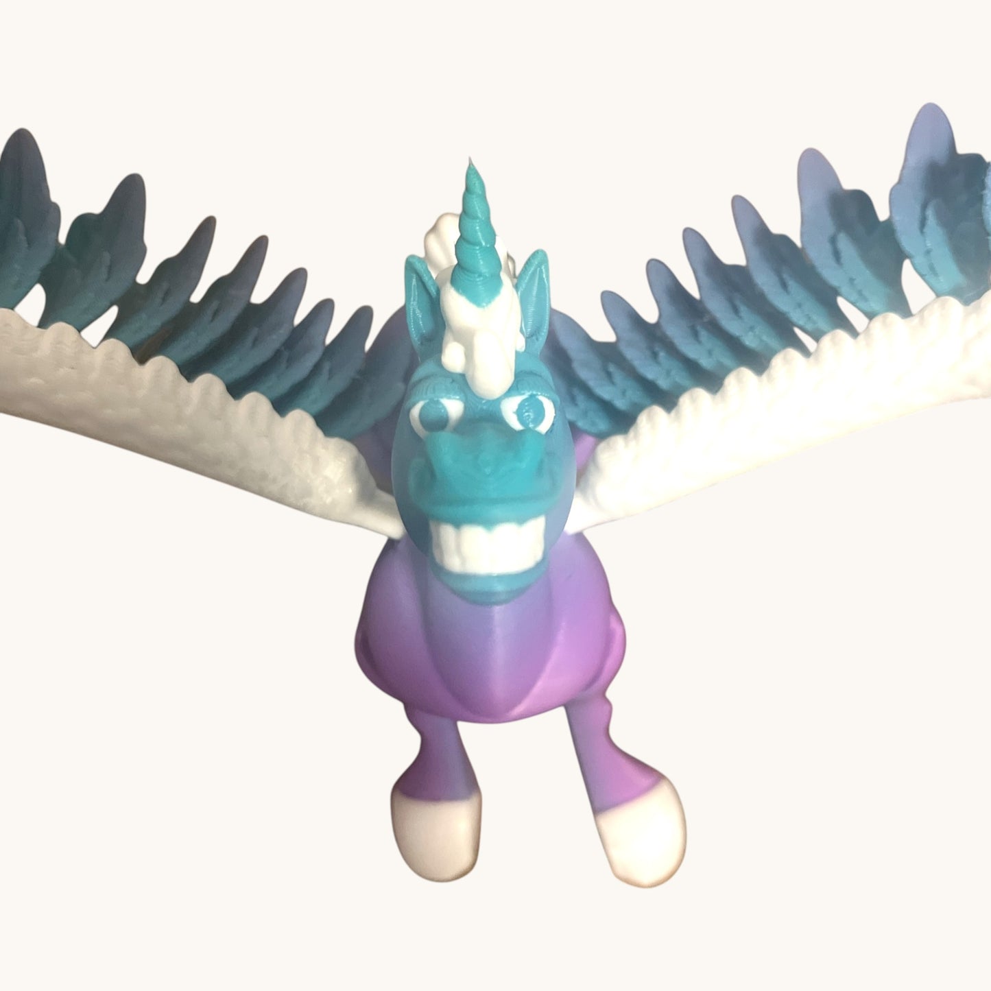 Flutterby Creations Flexicorn 3D printed toy unicorn, teal and purple with white and blue wings, toothy grin.